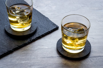 Whiskey with ice. To glasses of strong alcohol drink on grey stone background