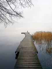 Selbstklebende Fototapeten Man standing alone on edge of pier and staring at lake. Mist over water. Foggy air. Early chilly morning in autumn. Beautiful freedom moment and peaceful atmosphere in nature. Back view. © Jani Riekkinen