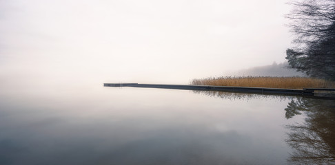 Foggy landscape with calm lake and wooden pier at tranquil autumn morning in Finland