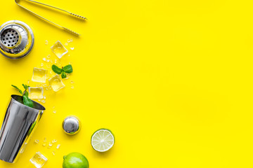 Bar background. Tools and ingredients for cocktails. Shaker, lime, ice on yellow background top-down frame copy space