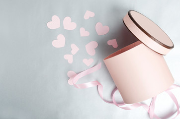 Top view of opened pink round box and little paper pink hearts on the silver surface.Concept of romantic presents.Empty space for text