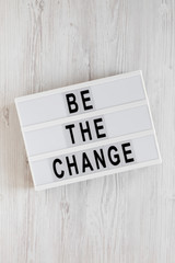 'Be the change' words on a lightbox on a white wooden background, top view. Overhead, from above, flat lay.
