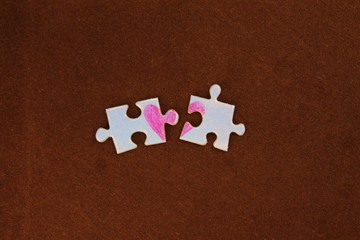 Puzzle with a red heart on the brown felt background. Two disconnected halves. Valentine's day stock photo with empty space for your text. For web, print, postcard, background and wallpaper