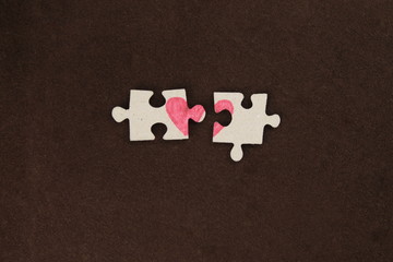Puzzle with a red heart on the brown felt background. Two disconnected halves. Valentine's day stock photo with empty space for your text. For web, print, postcard, background and wallpaper