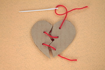 Broken cardboard heart on felt orange background. Two halves of the heart sewn together in red thread. The concept of a broken heart, unrequited love. Valentine's Day stock photo with empty space