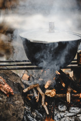 Camping cauldron with a lid from under which there is steam standing on the grill for cooking at...