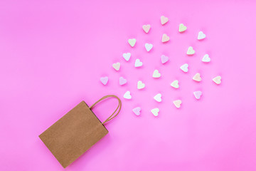 Gift bag with scattered hearts sweets on a pink background. Valentine's Day present concept. Top view, flat lay.