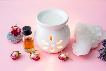 Obraz na płótnie Canvas White ceramic candle aroma oil lamp with essential oil bottle and dried flowers, crystal geodes on modern pastel pink and blue background indoors.