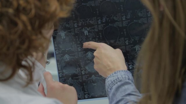 Two doctors examine patient’s abdominal tomography, stand with their backs to camera, study results, move their fingers over image, argue, indicate problems, treatment results, monitor disease, work