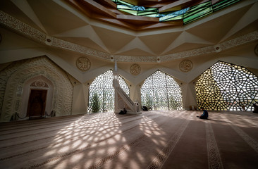 Local people praying inside the modern mosque. Sunlight shines through glass windows into the main...