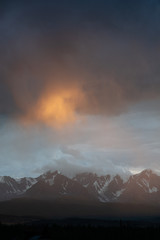 epic landscape of a giant snowy mountain range under a hurricane of rain and sun