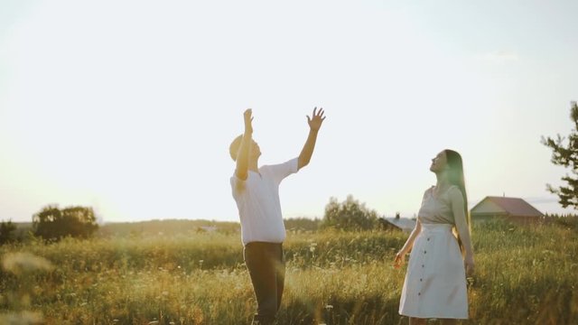 Lovers enjoy sunset time outdoors, they have fun and play. Happy young family in rural place, they throw a hat. Concept of strong family of millennials and their free time together