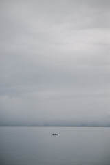 small boat on the water in the middle of a large clean lake in gray gloomy cloudy weather - 314422101