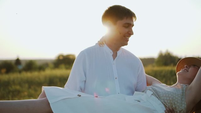 Happy millennials family outdoors, having fun at sunset in summer. Walking together, playing and enjoying. Guy moving around spinning his girlfriend, they laugh and smile