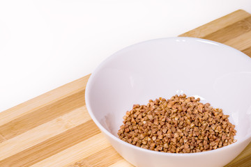 Buckwheat groats in a ceramic bowl on a white cement background. Healthy eating concept.