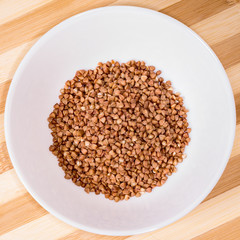 Buckwheat groats in a ceramic bowl on a white cement background. Healthy eating concept.