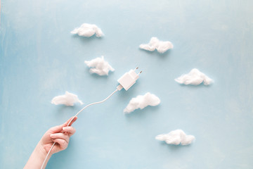 hand holds usb cable with charger like a kite flying into the sky with clouds, cotton and blue background, copy space, saving energy and saving natural resources concept