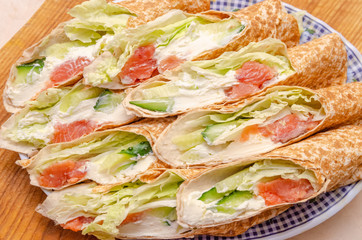 Tortilla rolls with salmon, tender cheese, lettuce and fresh cucumber close-up on a plate
