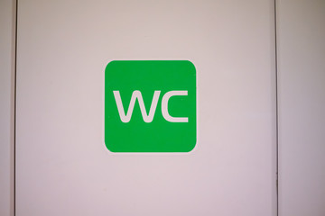Green WC toilet sign on white door close up with copy of space