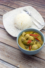 Green curry with fish balls and steamed rice on a wooden table