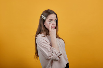 Disappointed caucasian woman in fashion pastel shirt keeping finger on cheeks, wipes away tears, crying isolated on orange background in studio. People sincere emotions, lifestyle concept.