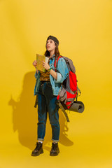 Dreamful looking up for way. Portrait of a cheerful young caucasian tourist girl with bag isolated on yellow studio background. Preparing for traveling. Resort, human emotions, vacation. Copyspace.