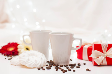 red gift boxes with ribbons, a pair of white cups and flowers on a white delicate background with bokeh.