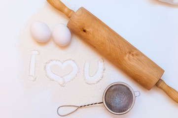 inscription i love you on flour. near a rolling pin, eggs and a sieve.