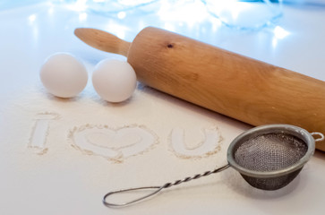 inscription i love you on flour. near a rolling pin, eggs and a sieve.