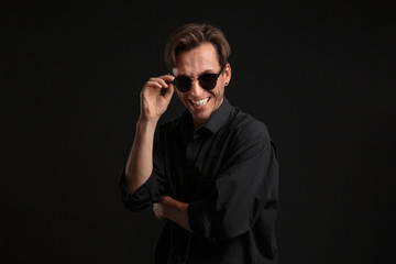 Confident stylish man in black eyeglasses isolated over black background.