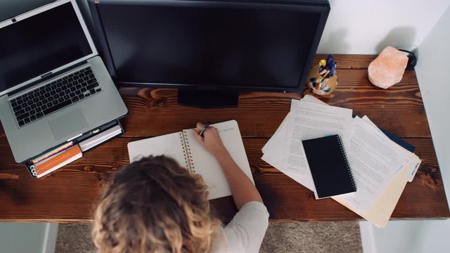 Overhead dolly of woman writing notes working at desk in daytime slow motion