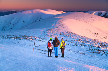 Three active hikers watching the sunrise scenery in winter landscape. Hiking together, teamwork in mountains, concept photo. Carpathian hills