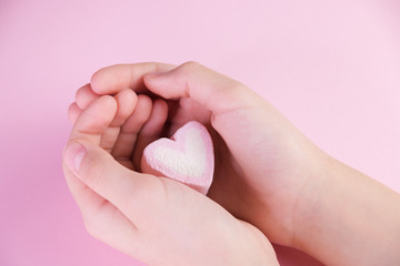 Pastel valentine background made of marshmallows souffle in the form of hearts on a pink background in hands. Valentine's Day concept with copy space