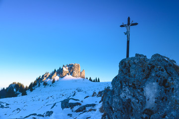 Cross on the rock in white winter nature under blue sky. Christianity photo, blue edit space