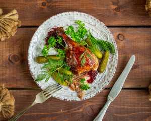 Baked duck leg with fresh aromatic herbs and pickled gherkins in a ceramic plate and Cutlery