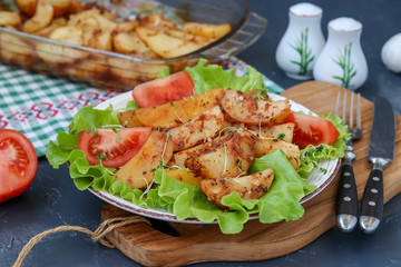 Baked potatoes and tomatoes with lettuce on a plate against a dark background, Horizontal orientation
