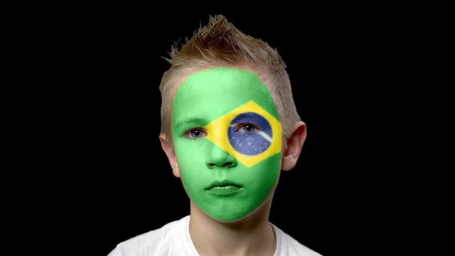 Sad fan of the football team of Brazil.. A child with a face painted in national colors. Unhappy boy with sad eyes. Fiasco of your favorite team. Disappointment. Sadness. Experience. Failure. Bad luck