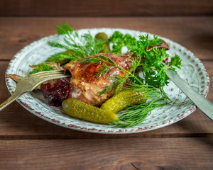 Baked duck leg served on a ceramic round plate with fresh herbs and pickles.