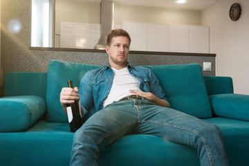 young handsome man sitting on the sofa with a bottle of wine drinking in the cozy living room home...