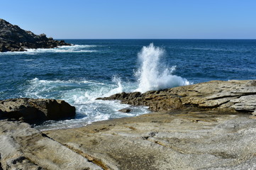 Seascape with waves breaking against the rocks and blue sky. Galicia, Spain.