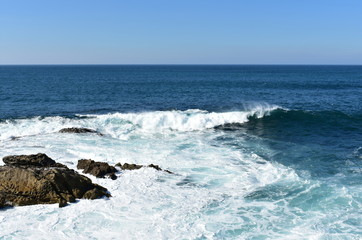 Seascape with waves breaking against the rocks and blue sky. Galicia, Spain.