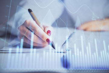 Double exposure of woman's hands making notes with forex graph hologram. Concept stock market...
