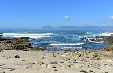 Wild small beach with rocks and waves breaking. Bay with mist and blue sky. Baroña, Spain.