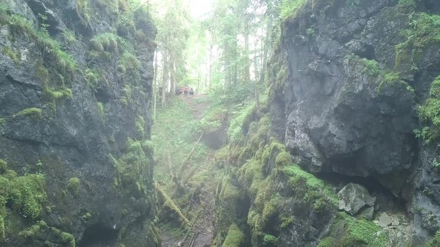 People on steep rocky cliffs covered by green moss in morning fog. Stock footage. Aerial of the deep gorge between two mountain slopes in the forest.