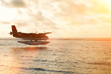 Summer sunset with seaplane. Landing seaplane on the dawn seashore. Calm scenery on evening sea.