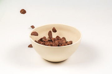 Chocolate corn flakes falling to the white bowl isolated on white. Motion.