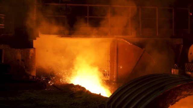 The blast furnace with flowing liquid metal and flying sparkles. Stock footage. Close up of the hot metal production at the factory, heavy industry concept.