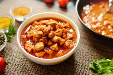 Tikka Masala. Chicken in tomato sauce in a white bowl. Spices and cherry tomatoes with parsley. Tasty chicken meat on a dark background. 