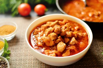 Tikka Masala. Chicken in tomato sauce in a white bowl. Spices and cherry tomatoes with parsley. Tasty chicken meat on a dark background. 