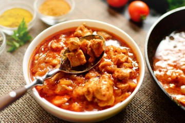 Indian food. Chicken Tikka Masala in a white bowl with spoon, on a dark background. Appetizing meat with tomato sauce, gravy. Food close up 